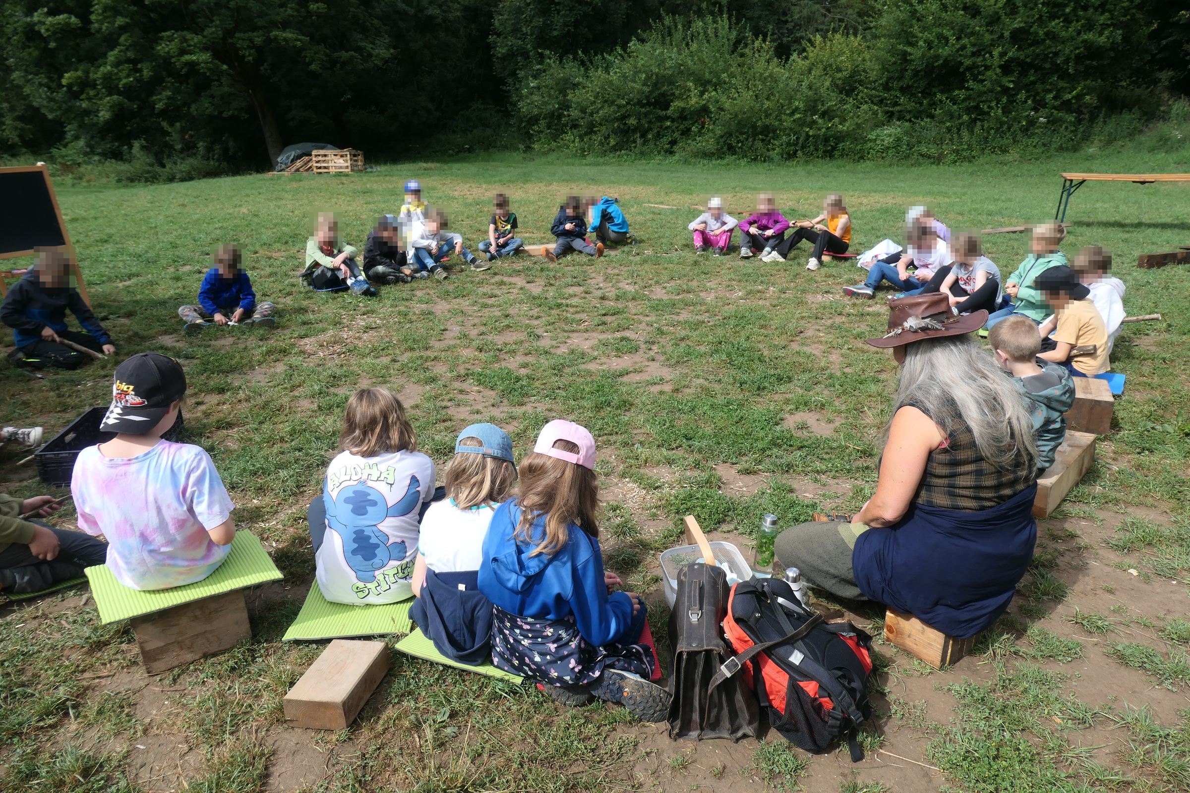 Kinder im Sitzkreis beim Naturcamp der Clément Stiftung auf einer Wiese